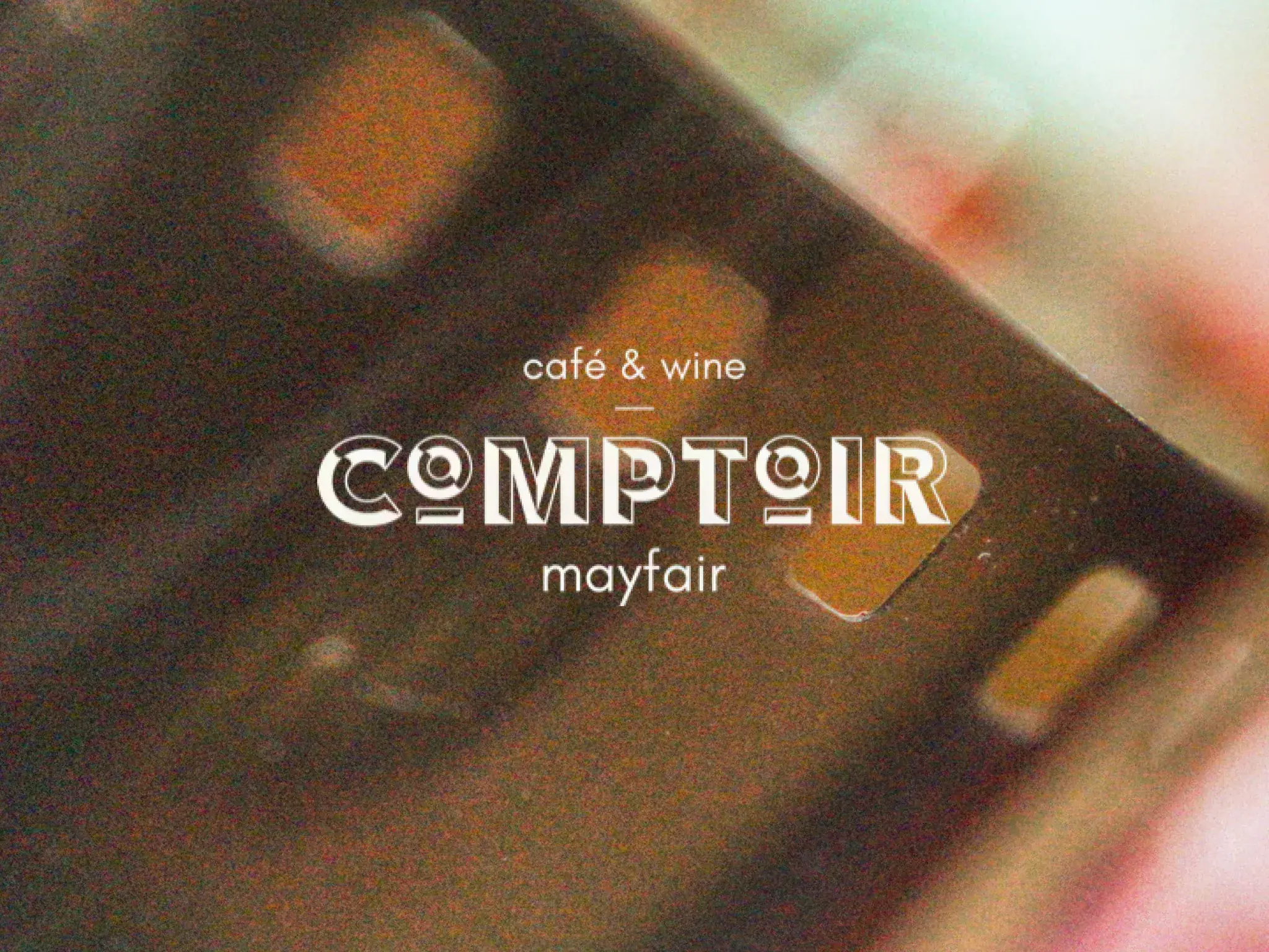 The Comptoir logo, “café & wine, mayfair”, over a grainy close-up of a film strip in warm light