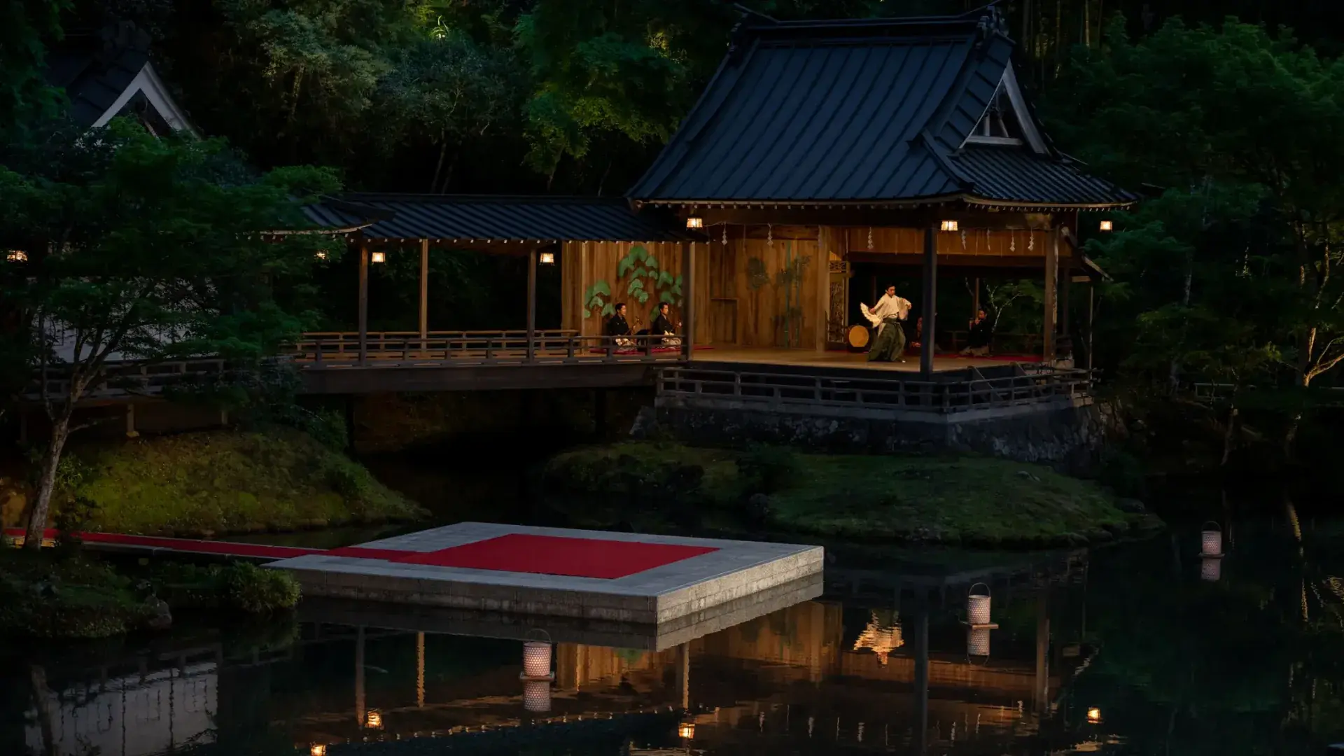 A traditional wooden stage at dusk, a dancer and musicians performing, its lanterns reflected in a garden pond